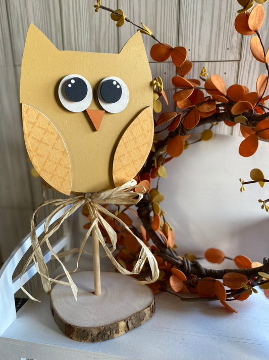 Hand-painted golden fall yellow owl with black/white bright eyes, and a raffia bow at the neck, standing on a wooden base.
