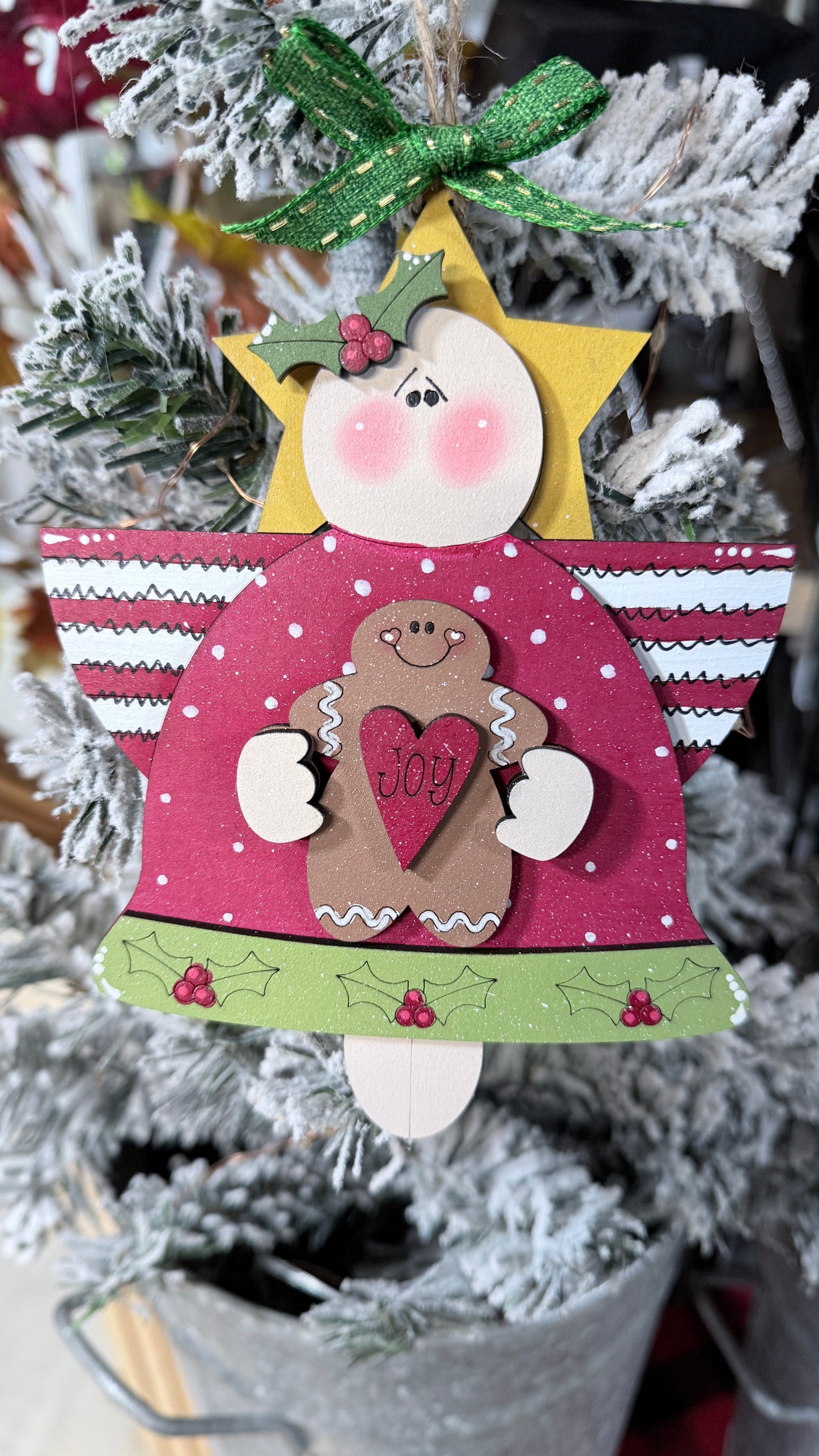 Decorative angel ornament with a gingerbread man and 'Joy' message on a Christmas tree.