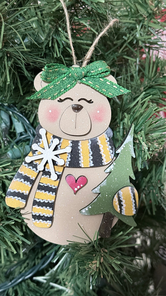 Decorative bear ornament with a striped scarf and green bow on a Christmas tree.