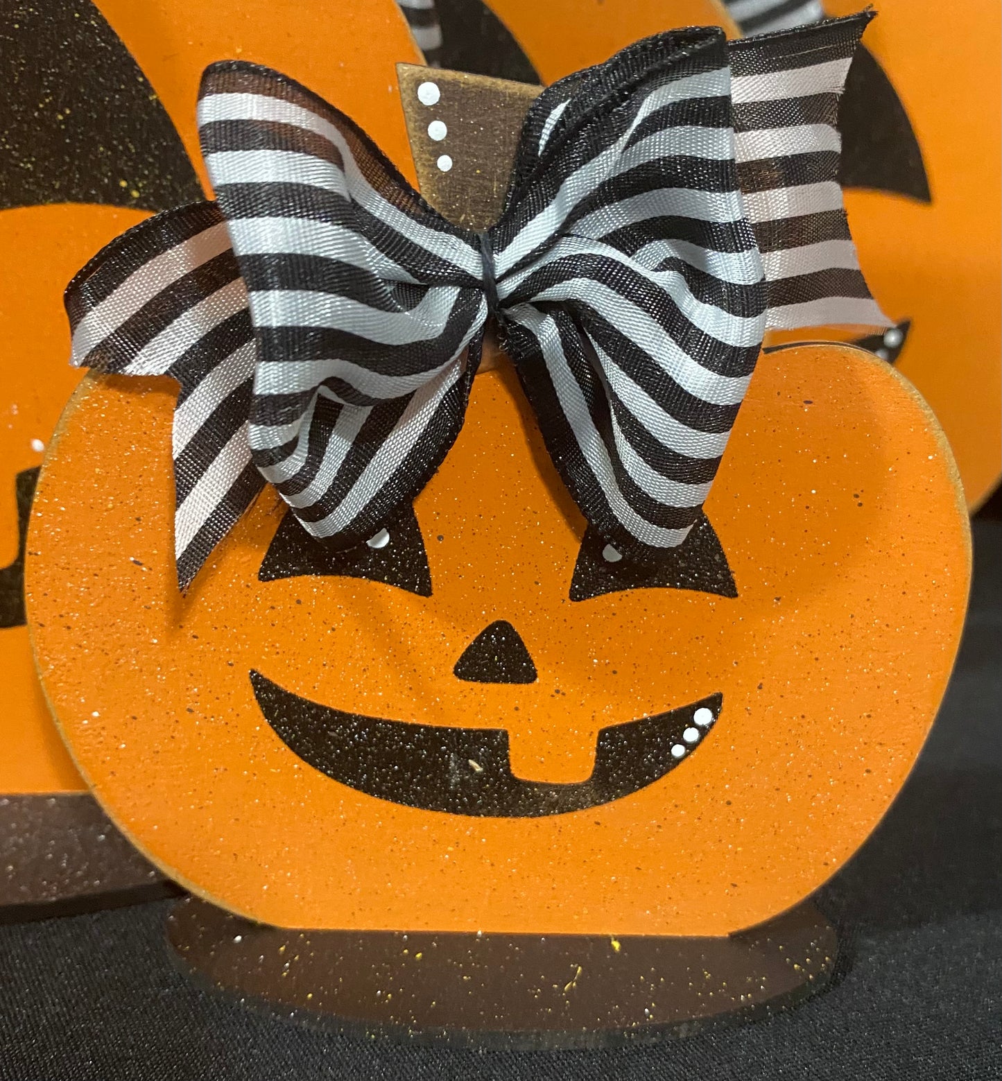 A small orange Jack-O-Lantern decor with a black whimsical face drawing and a black and white striped bow on top.