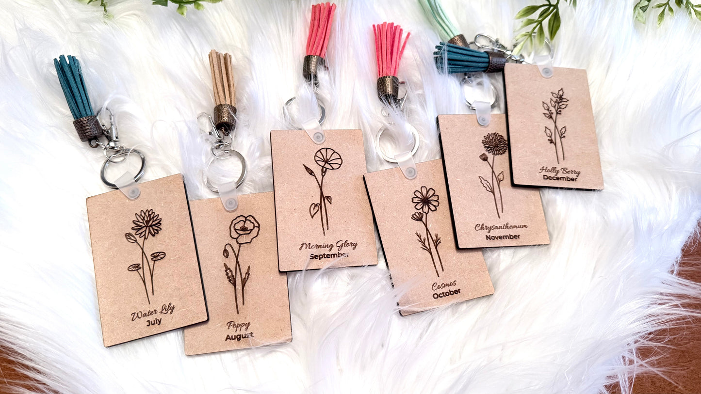 Birthday Key Chains are very popular. Each is engraved with the flower of the month, displayed the month and flower name. Each has a rustic colorful tassel to bring a pop of color and cheer to each piece. Shown on a white background.