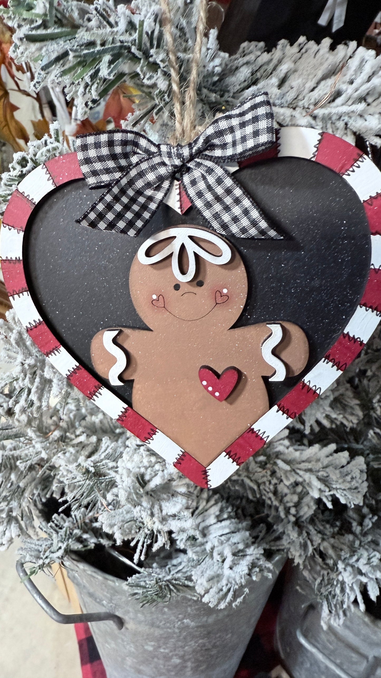 Heart-shaped gingerbread man ornament with a checkered ribbon on a Christmas tree.