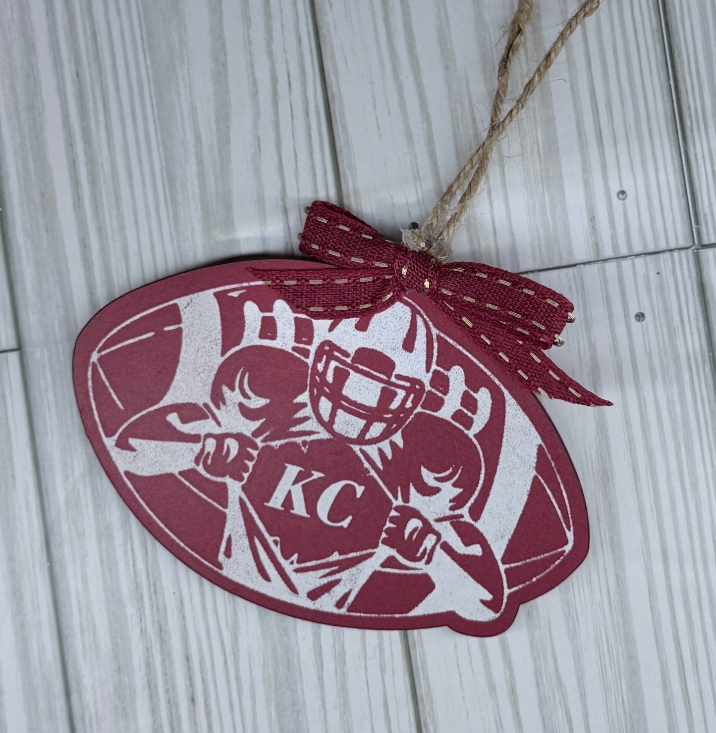 KC Football Ornament features a red background, stenciled artwork of a football player opening his jersey to reveal the letters KC.