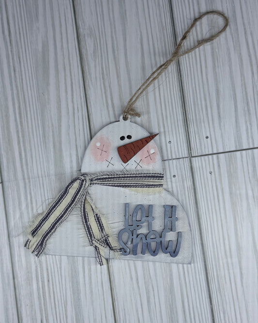 Decorative snowman ornament with 'Let is Snow' text on a wooden surface