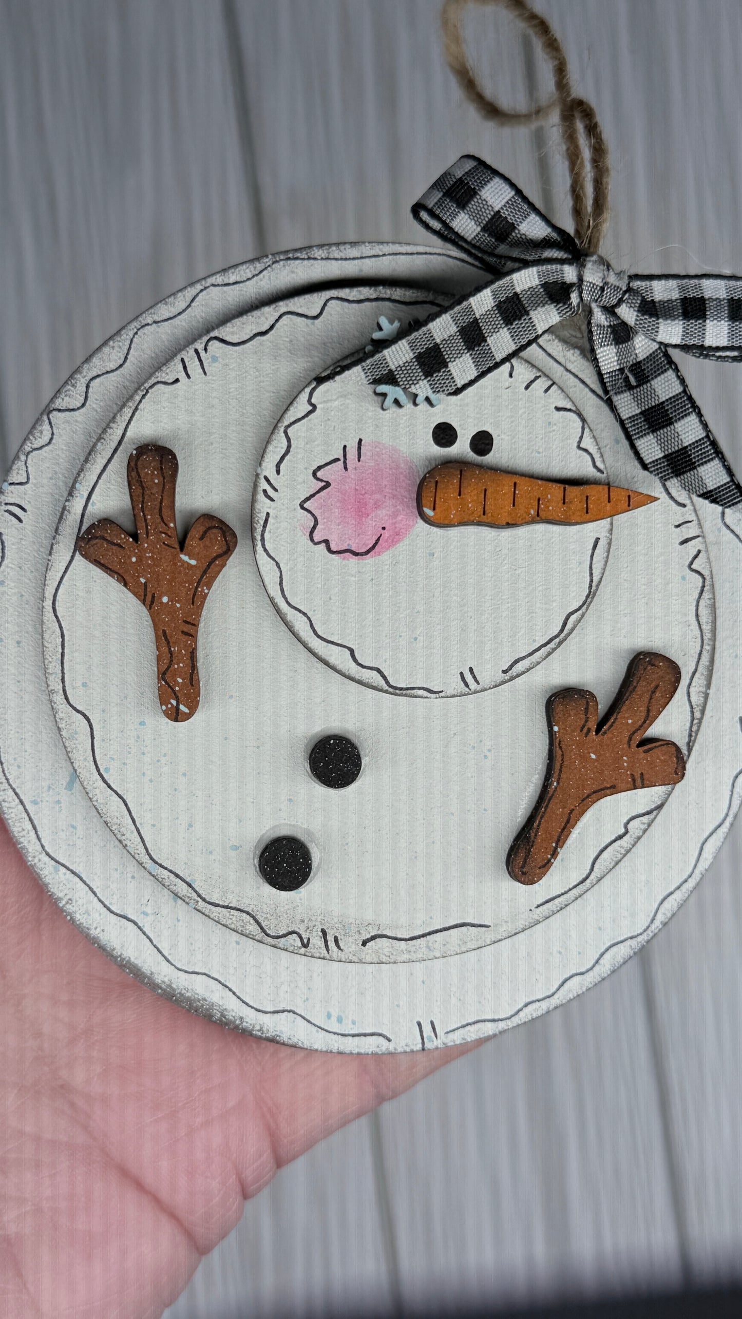 Handmade snowman ornament with a checkered ribbon on a neutral background. This ornament is what happens as the snow begins melting