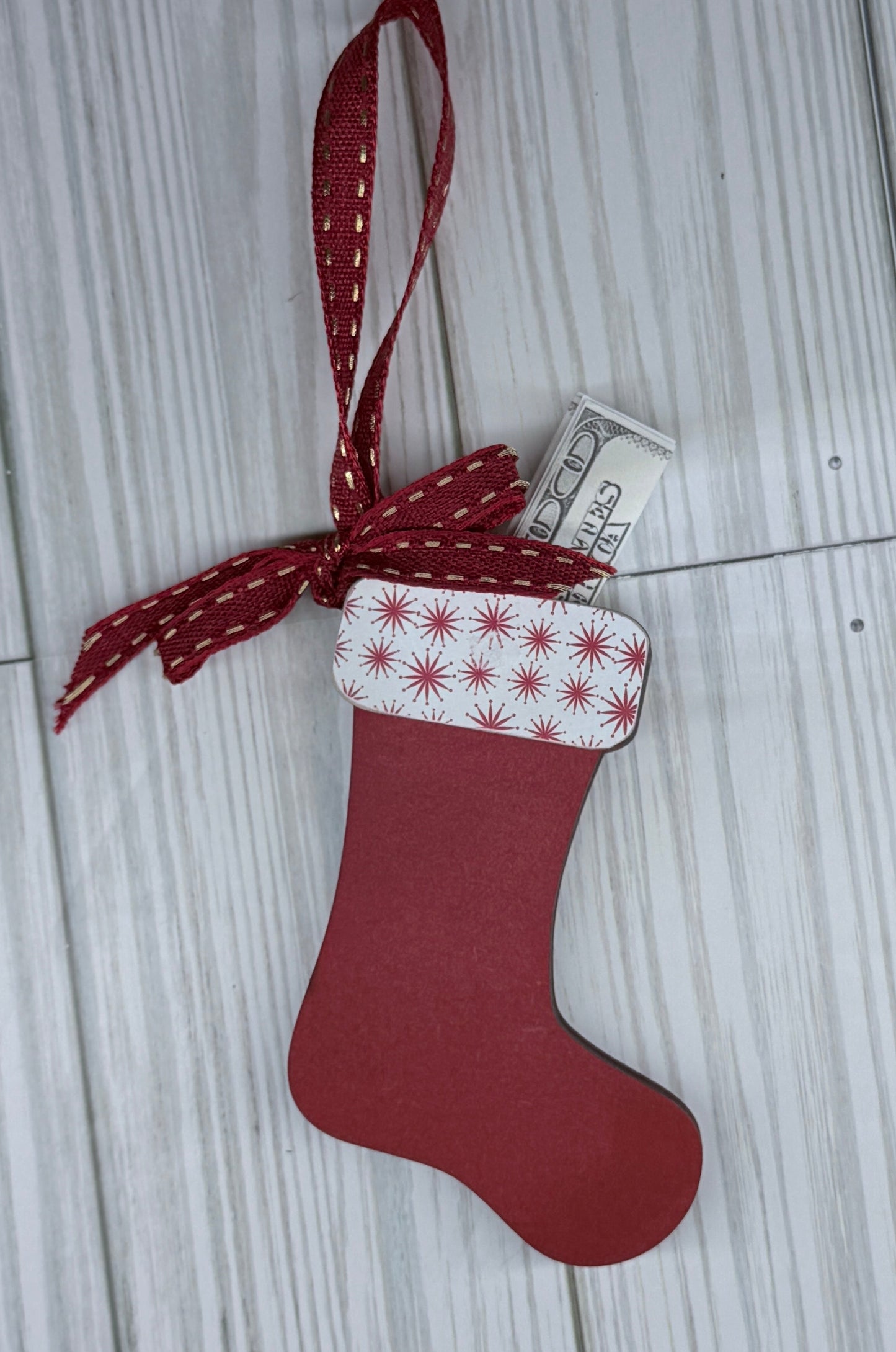 Small red Christmas stocking with a white and red patterned top on a light wooden floor. Red and gold bow and hanger