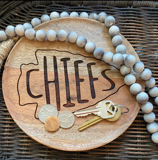 Wooden tray with 'CHIEFS' engraving, keys, and coins on a woven surface