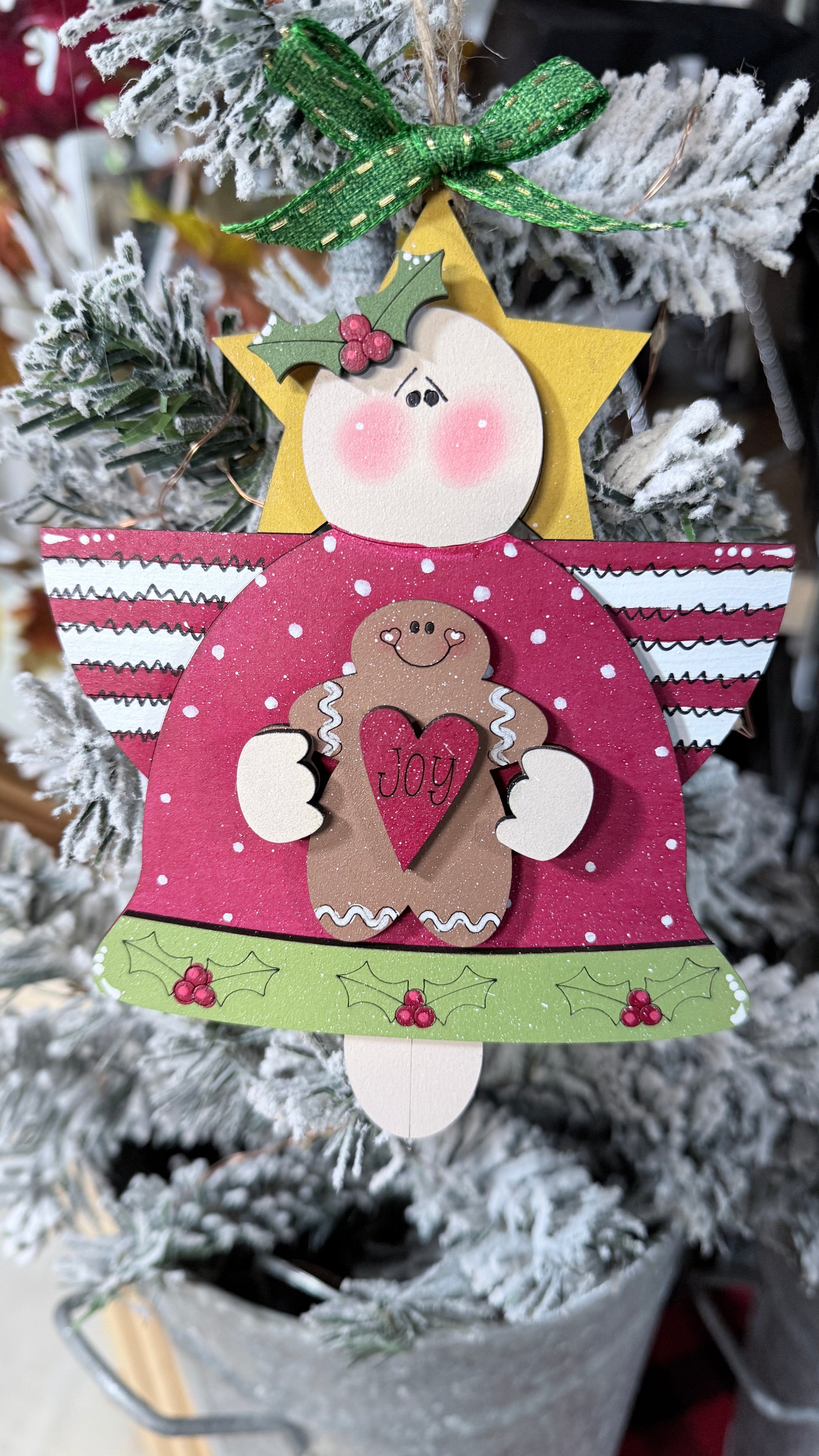 Decorative angel ornament with a gingerbread man and 'Joy' message on a Christmas tree.