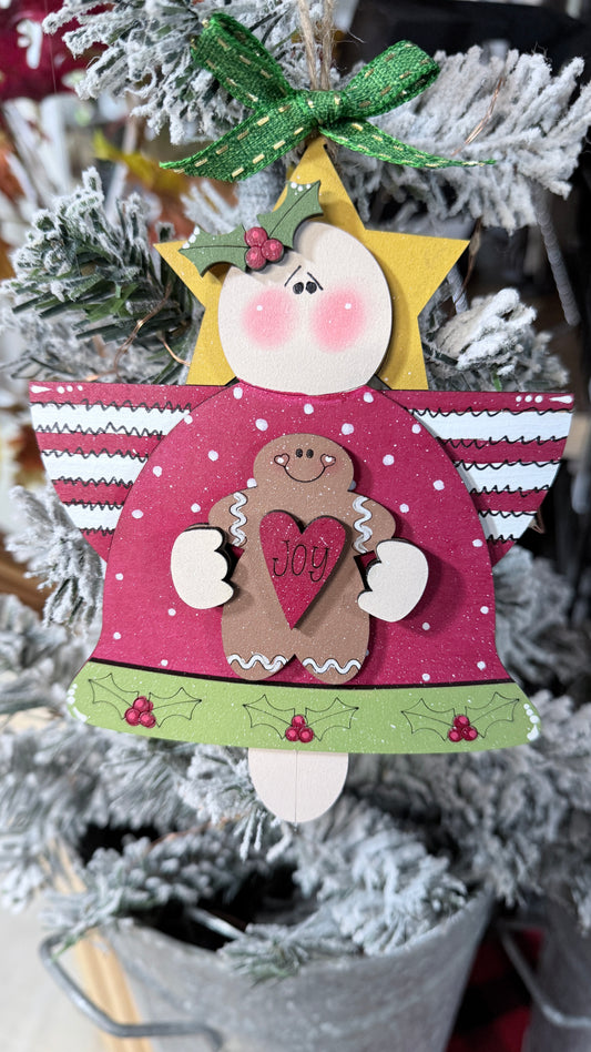 Decorative angel ornament with a gingerbread man and 'Joy' message on a Christmas tree.