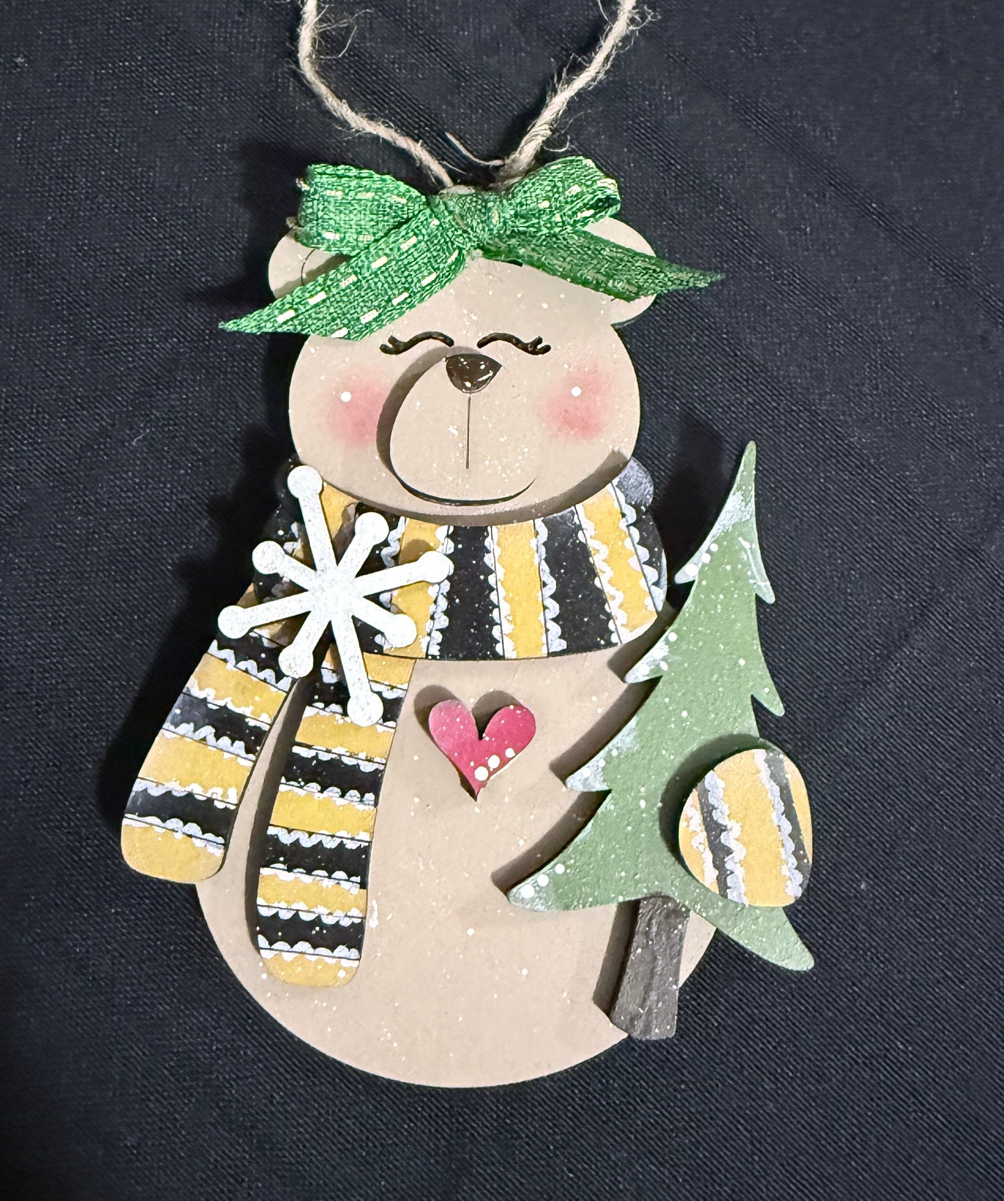 Decorative hanging tree ornament of a whimsical bear holding a tree.  His mittens and scarf are striped gold and black adorn with a snowflake.  It is hand painted & made of high grade MDF,    