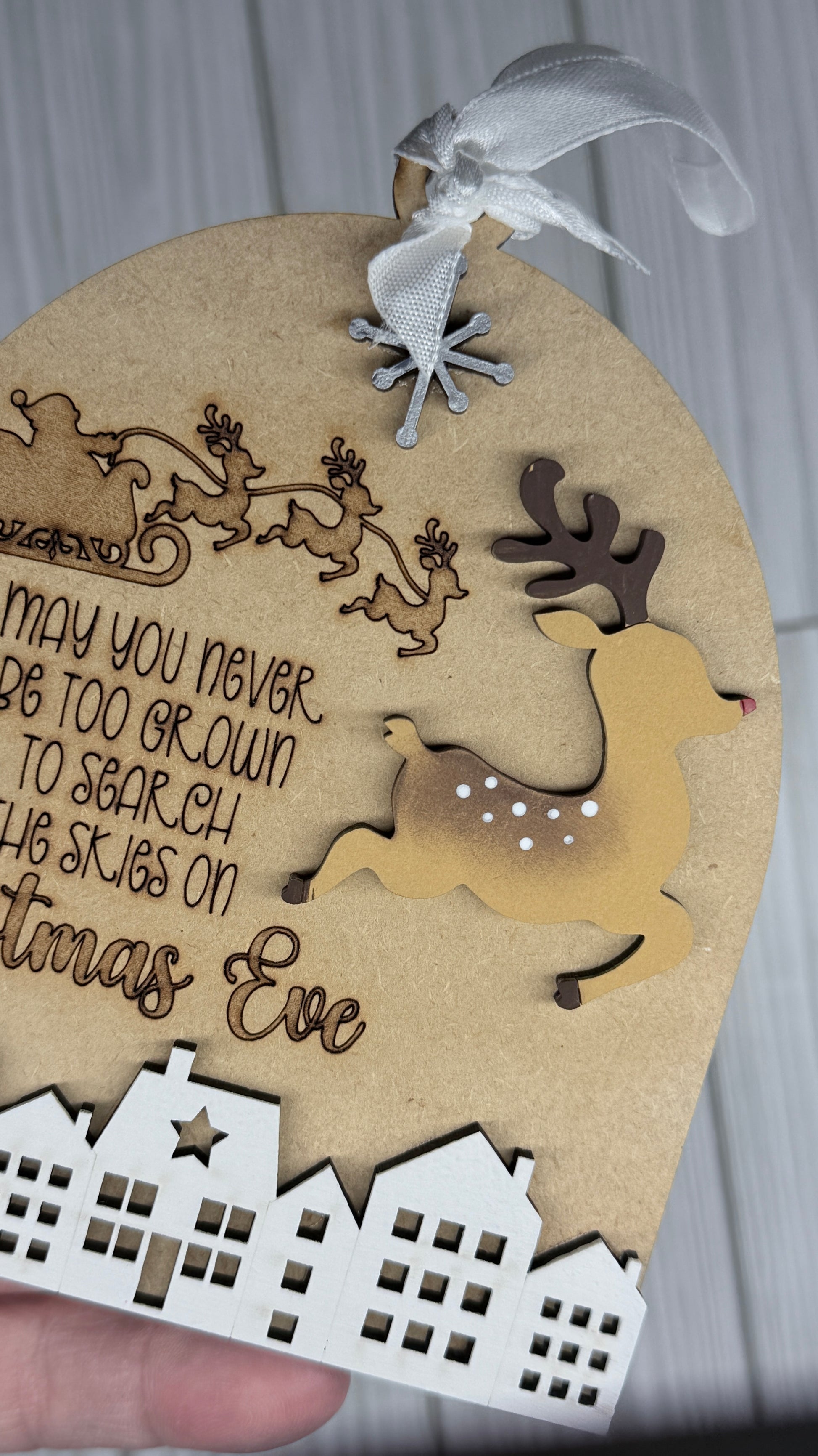 Decorative Christmas ornament with reindeer, sleigh, and text on a neutral background.  Closeup on the paint on the lead reindeer.  