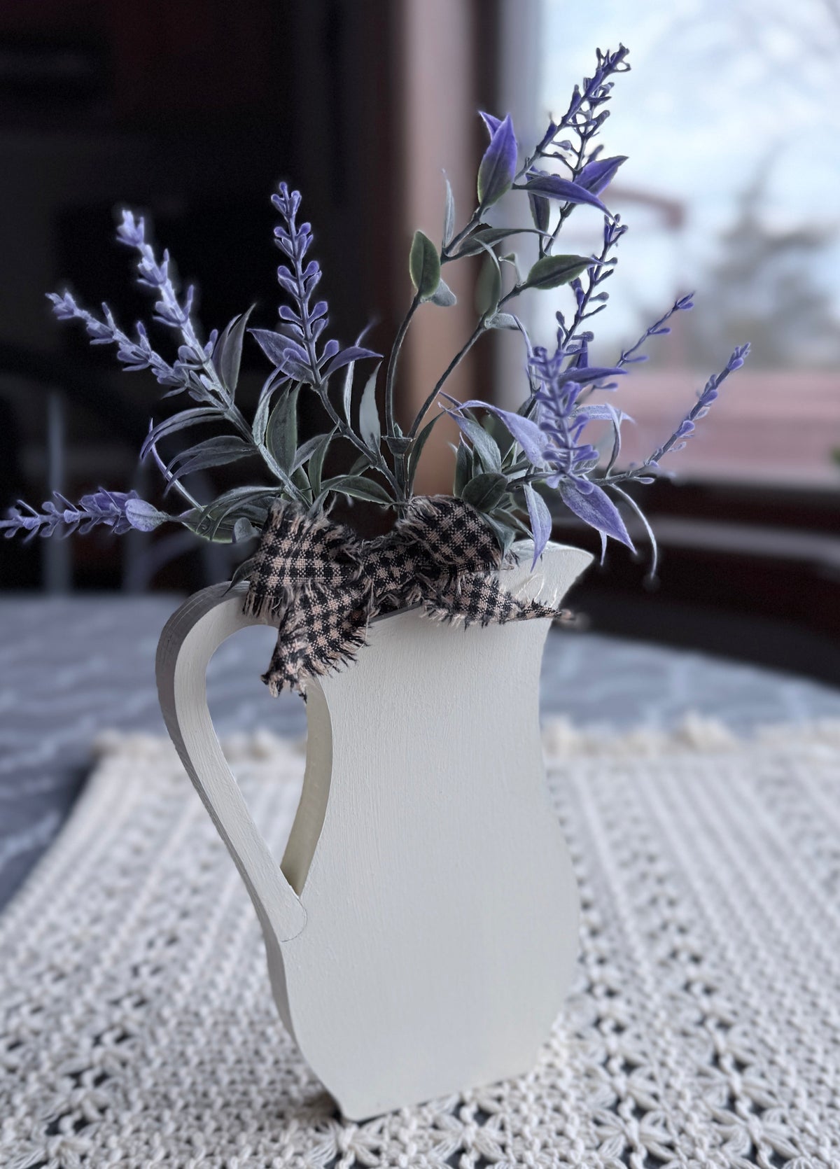 White pitcher with lavender and greenery on a lace tablecloth