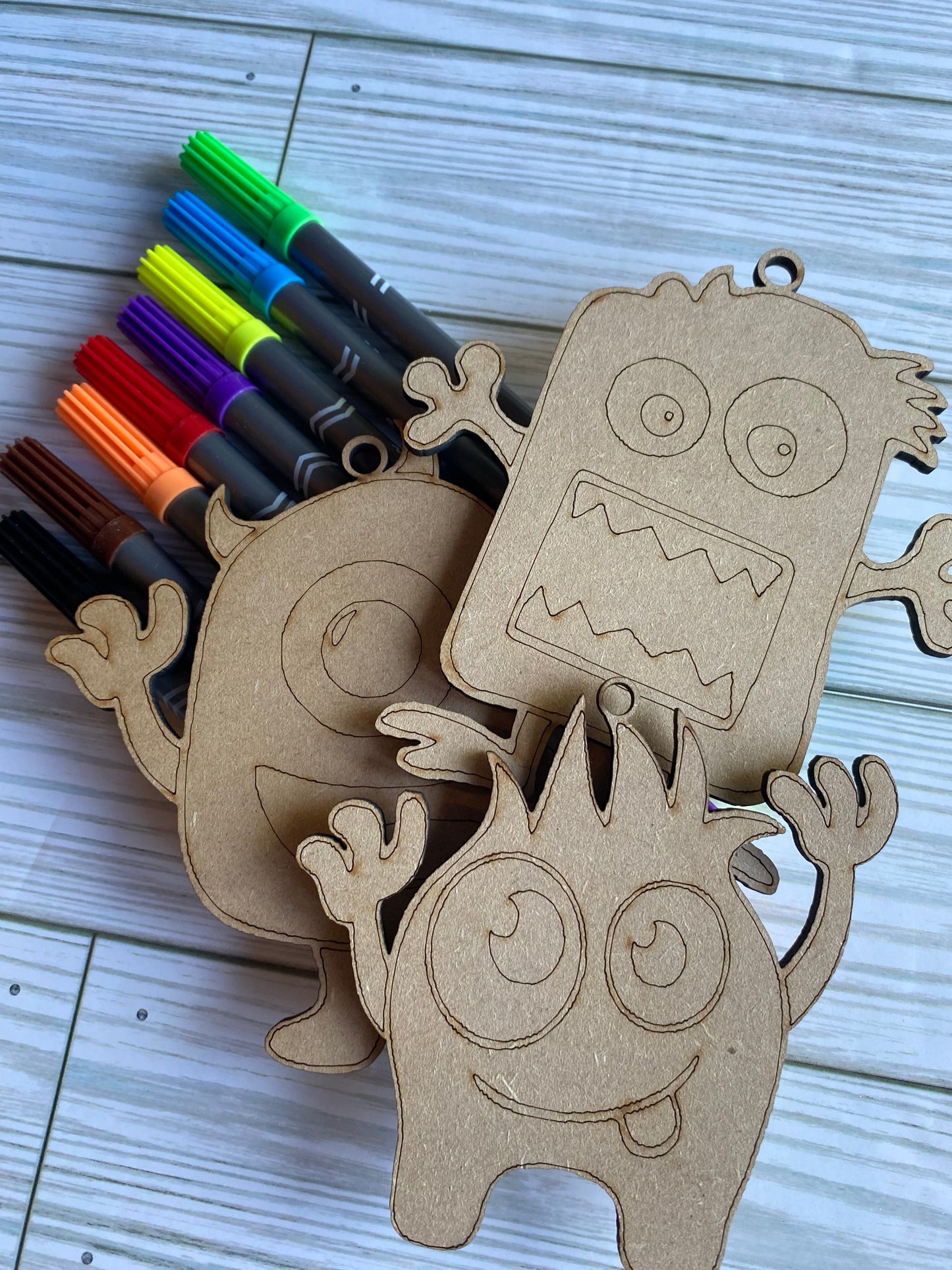 Three wooden monster shapes designed for painting and crafts, displayed with colorful markers and paints.