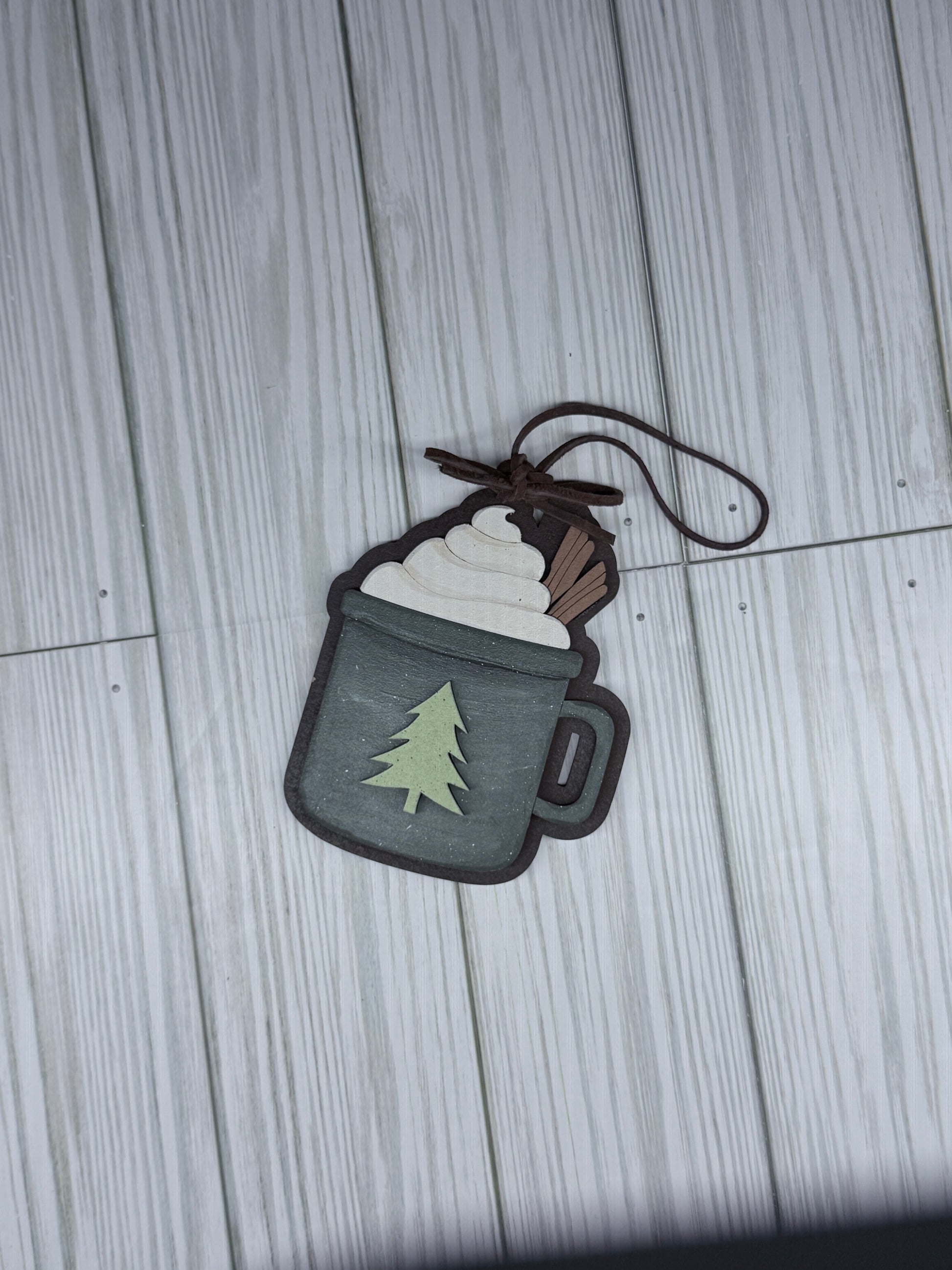 Mug ornament with a  tree on the mug. leather bow and hanger on reustic surface. 