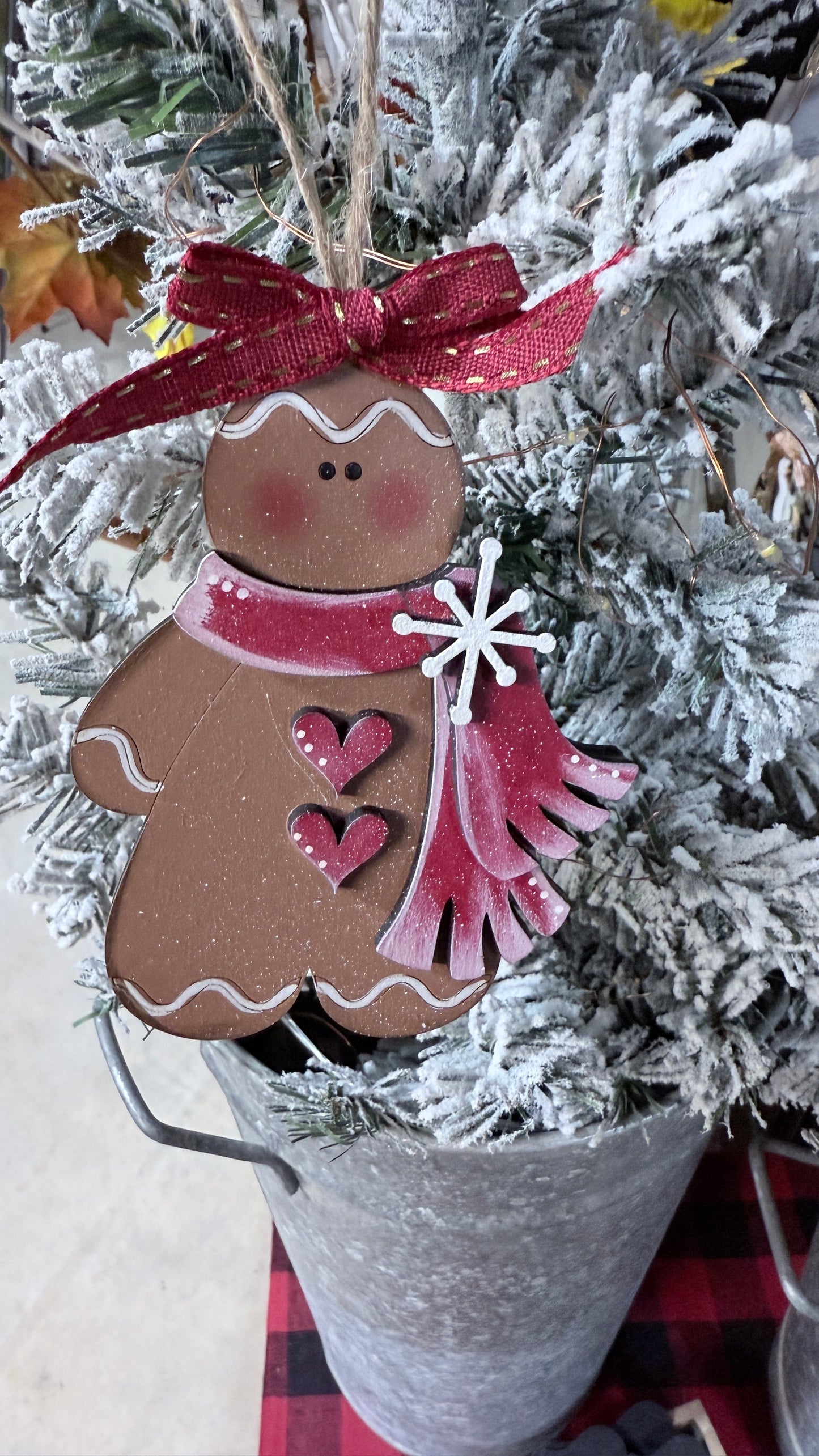 Decorative gingerbread man ornament with a red scarf and red bow on a Christmas tree.