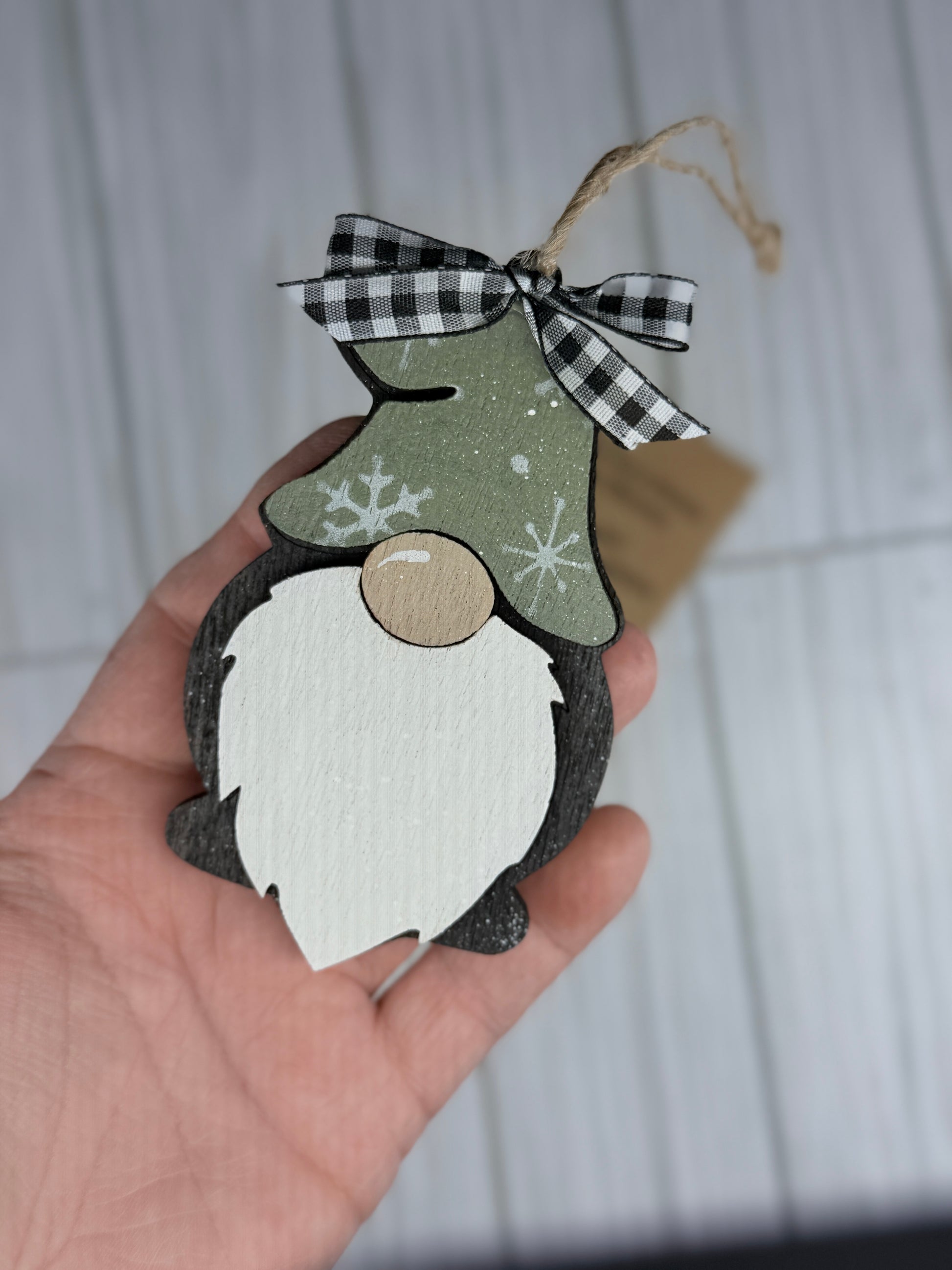 Hand holding a decorative gnome ornament with a checkered ribbon against a neutral background. Each gnome comes with a gnome/Home Poem. 