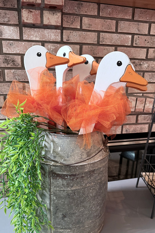 Decorative ducks with orange ribbons in a metal container against a brick wall.