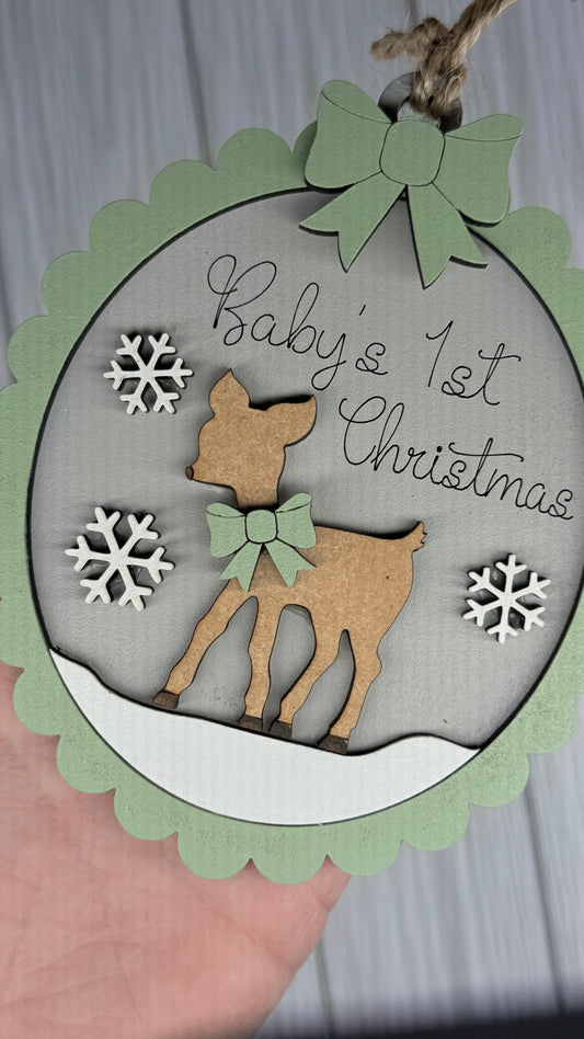 Decorative ornament with a deer and 'Baby's 1st Christmas' text, held by a hand.