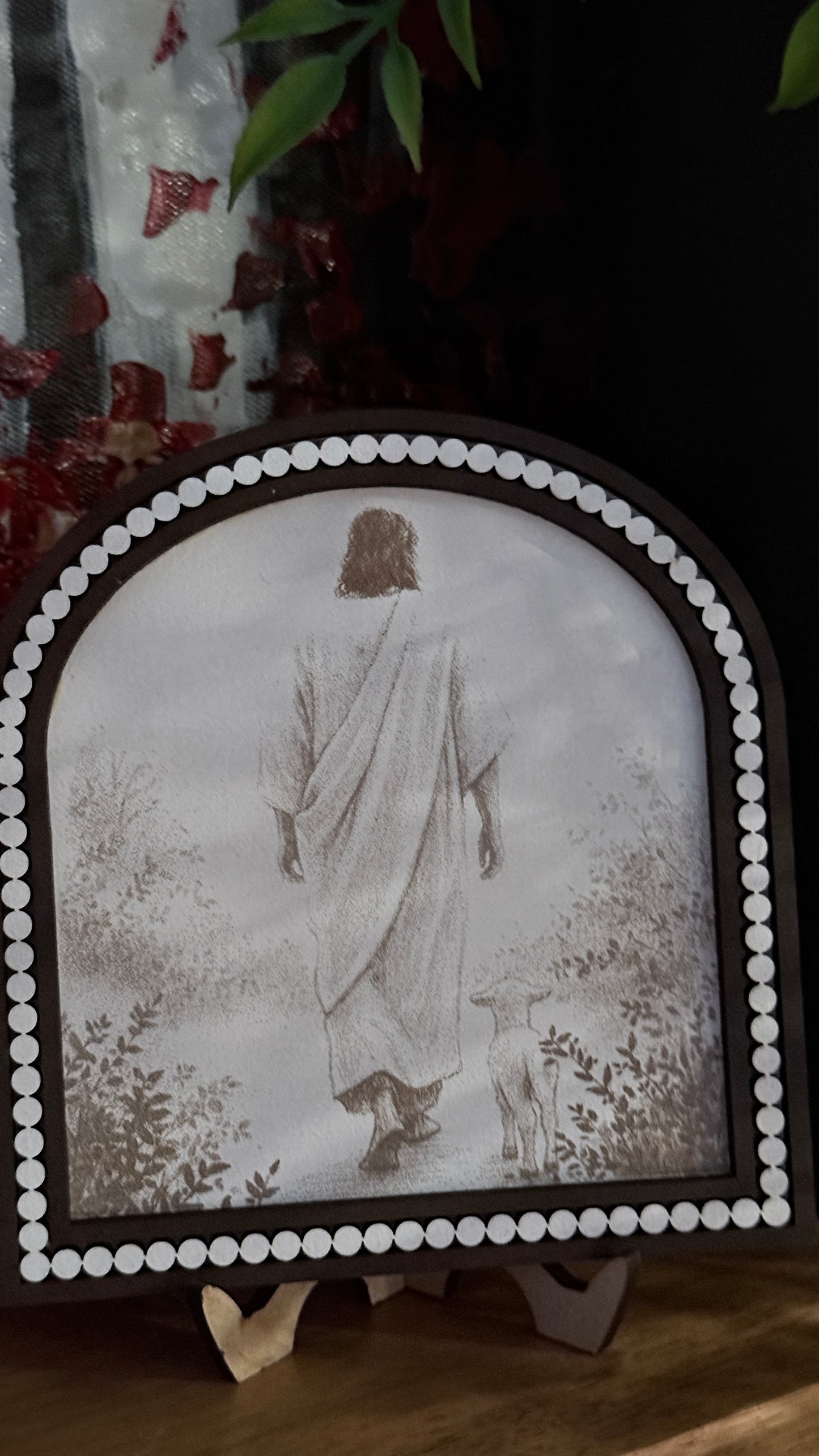 Decorative plaque with Jesus in a white robe and headscarf walking with the lamb. 