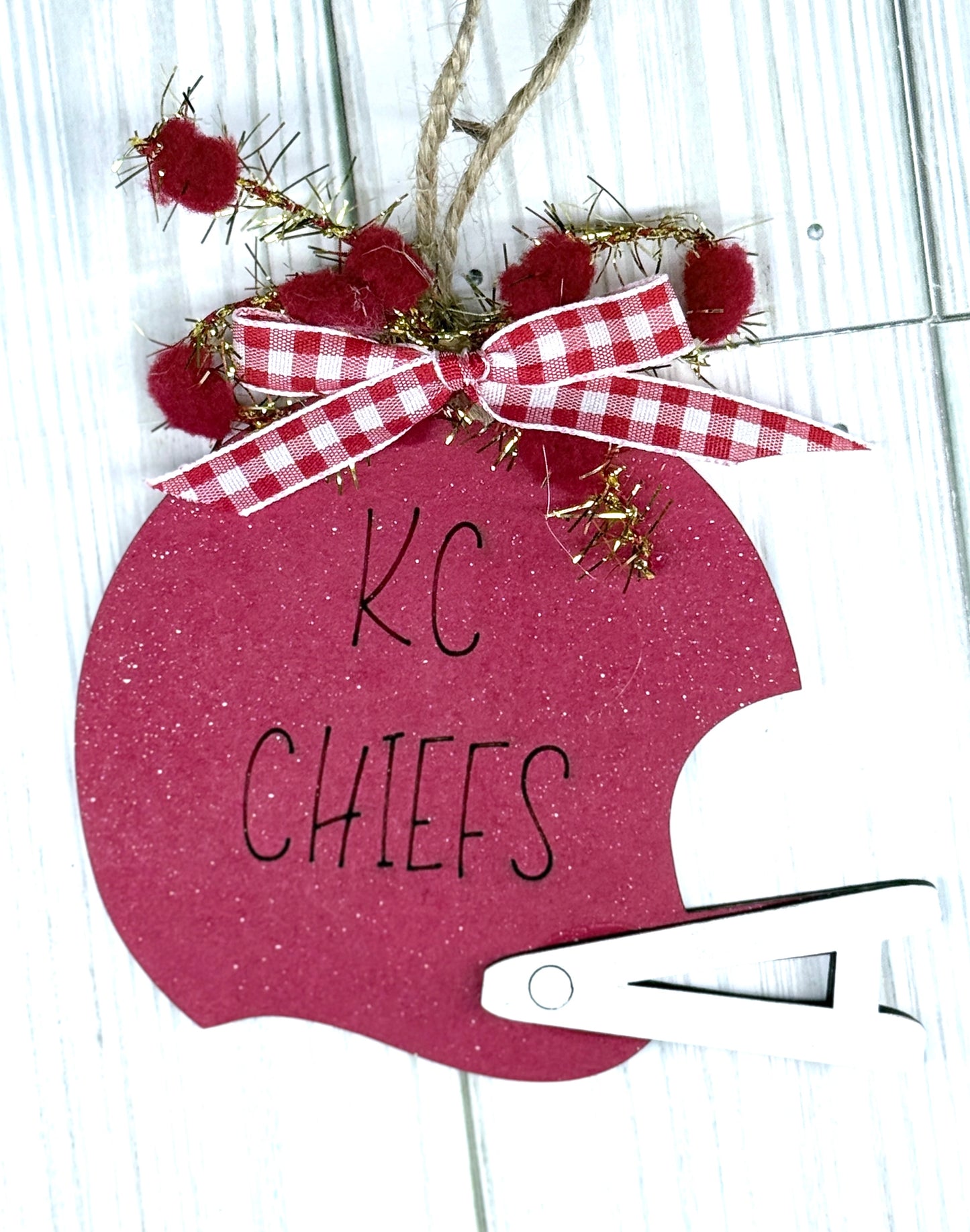 Decorative ornament shaped like a football helmet with 'KC Chiefs' text, red pom-poms, and a checkered ribbon.