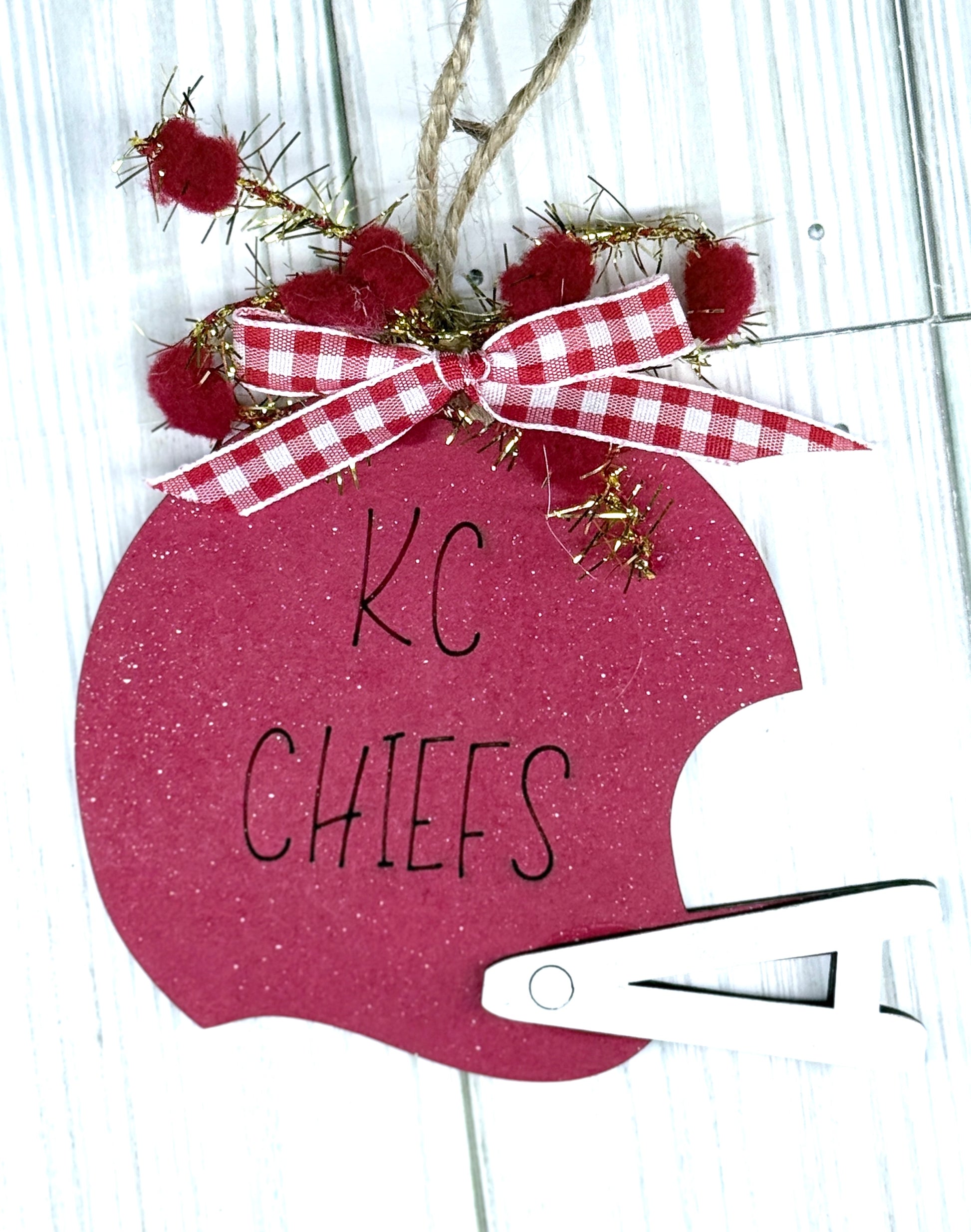 Decorative ornament shaped like a football helmet with 'KC Chiefs' text, red pom-poms, and a checkered ribbon.