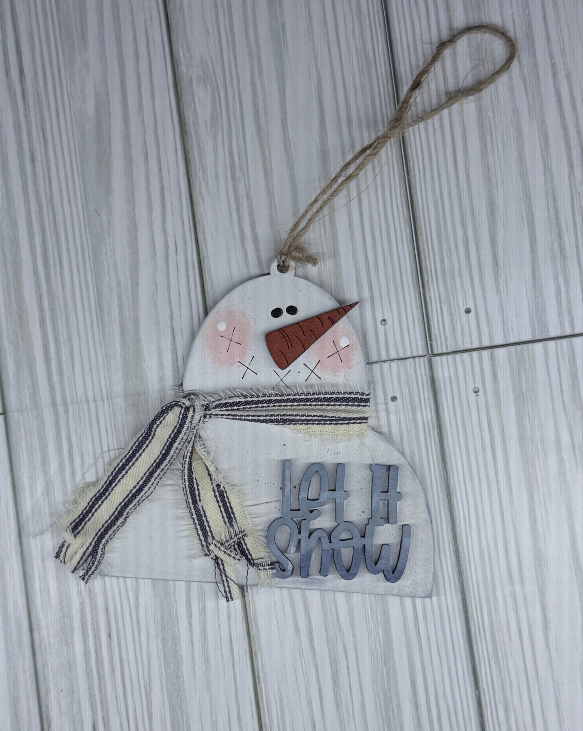 Decorative snowman ornament with 'Let is Snow' text on a wooden surface