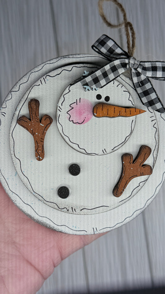 Handmade snowman ornament with a checkered ribbon on a neutral background.  This ornament is what happens as the snow begins melting   