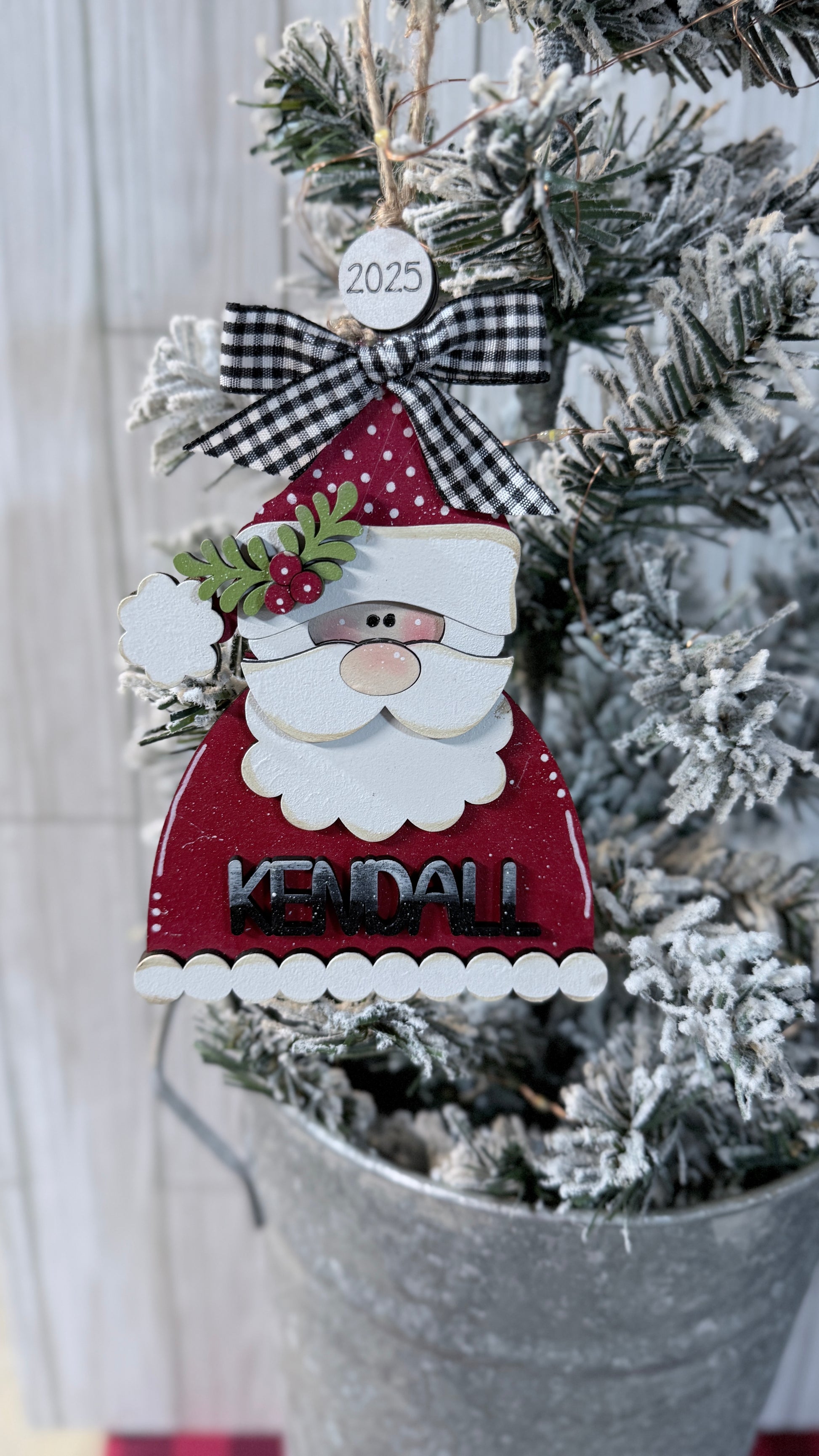 Decorative Santa Claus ornament with a checkered bow on a Christmas tree. Kendall on front.
