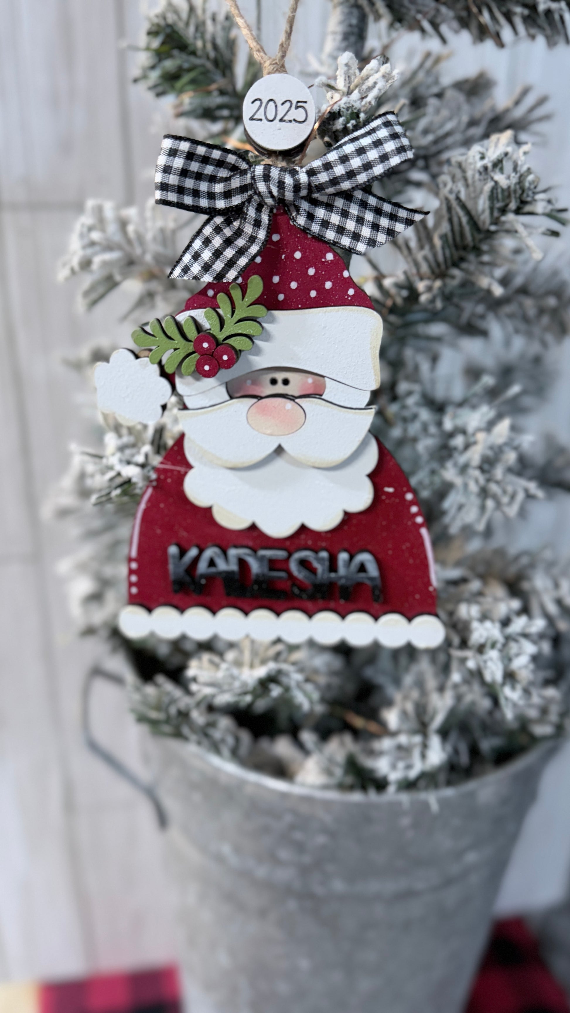 Decorative Santa ornament with a checkered bow and '2025' hanging on a Christmas tree.