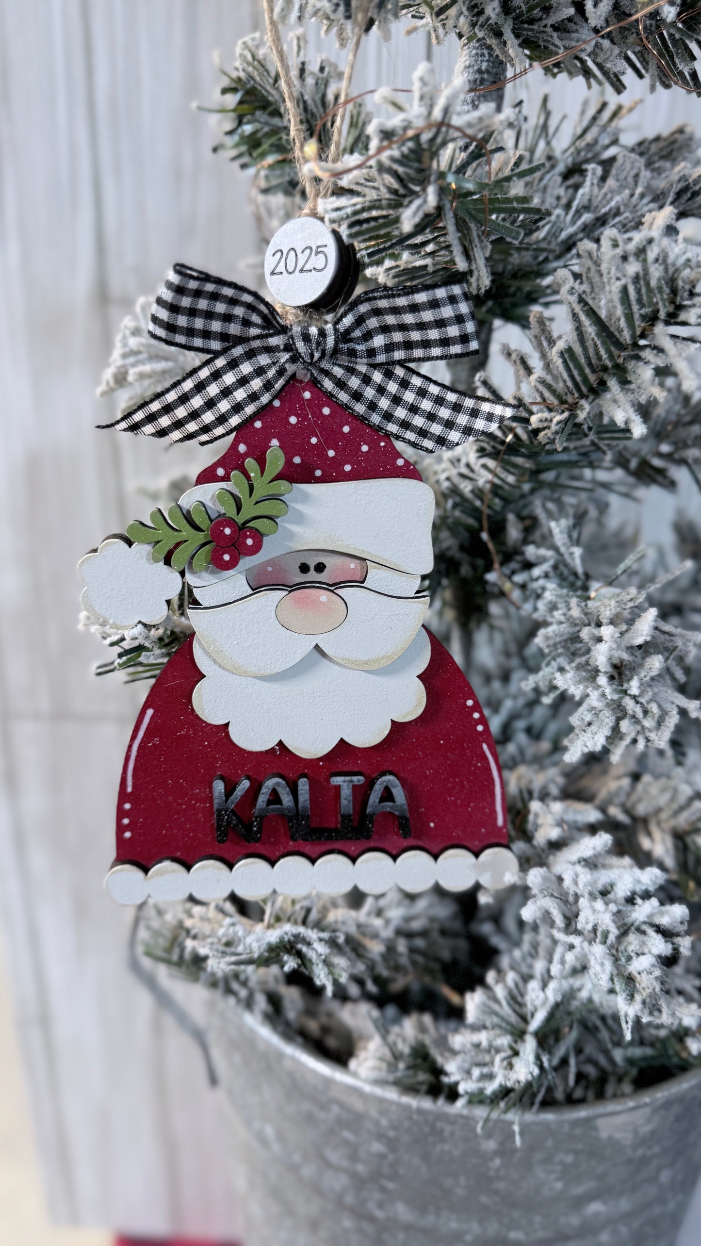Decorative Christmas ornament of a Santa Claus figure with a checkered bow hung on a tree.