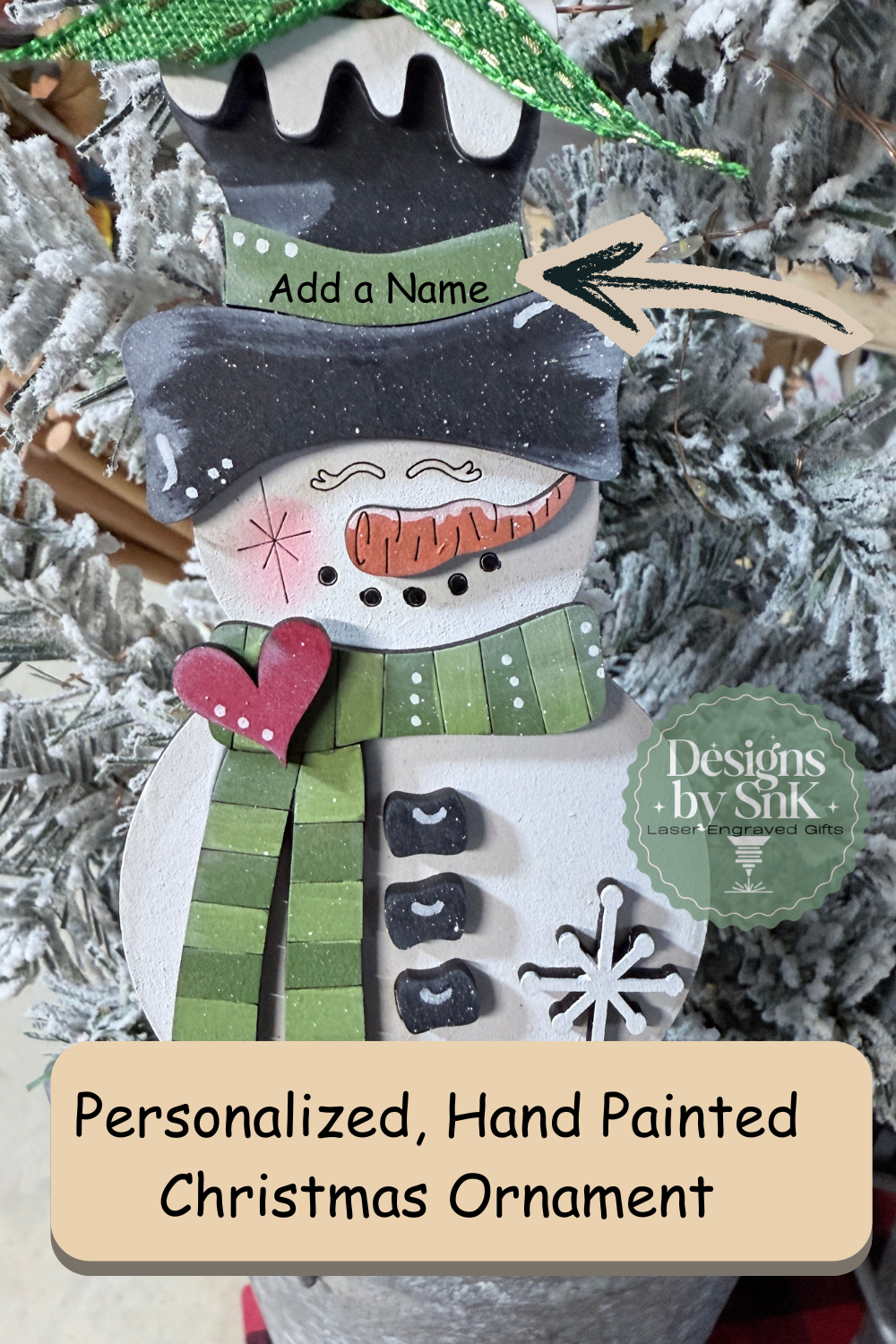 Personalized hand-painted snowman ornament with green scarf,  customizable name on brim of hat, hung on a Christmas tree.