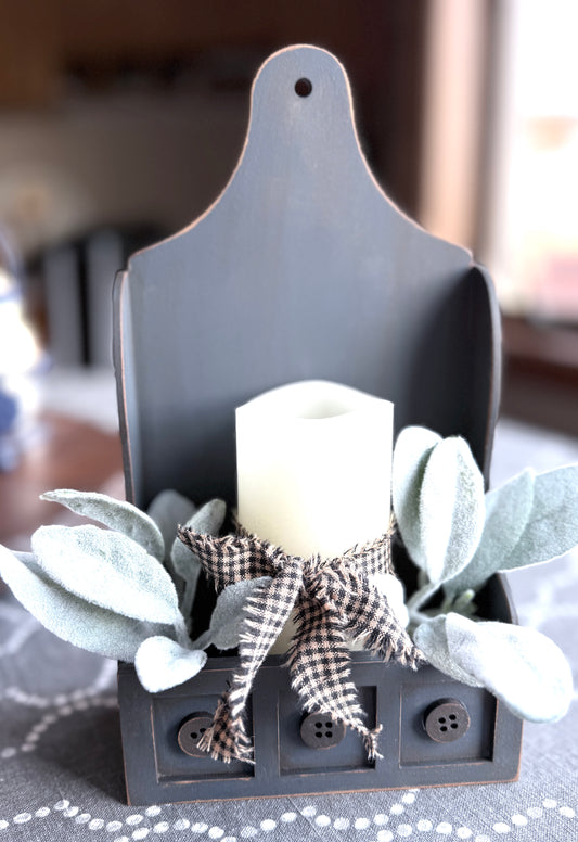 Decorative arrangement with a candle, leaves, and a checkered bow on a dark surface.