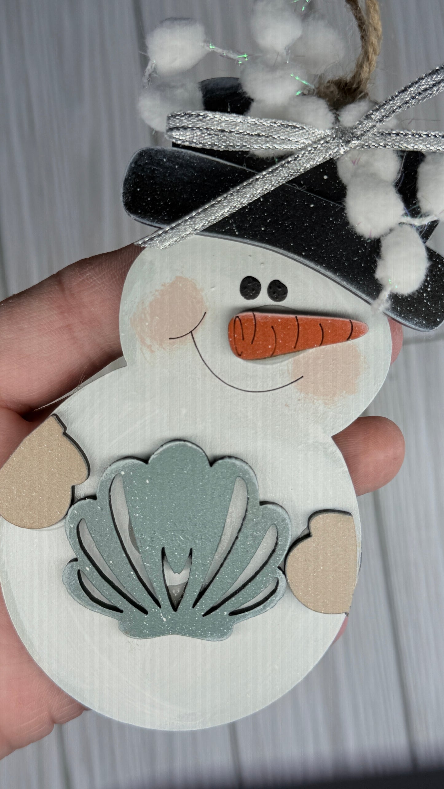Hand holding a snowman-shaped ornament with a shell design on a white background