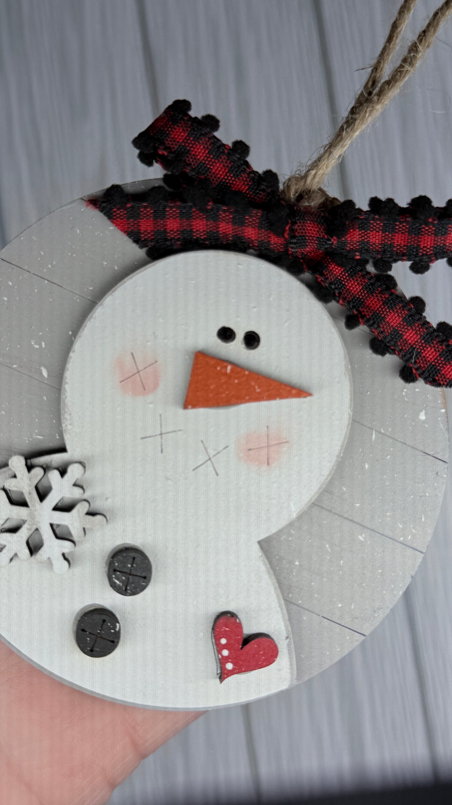 Shiplap Round ornament with snowma, adorn with buttons and heart. Features a red and black plaid bow.