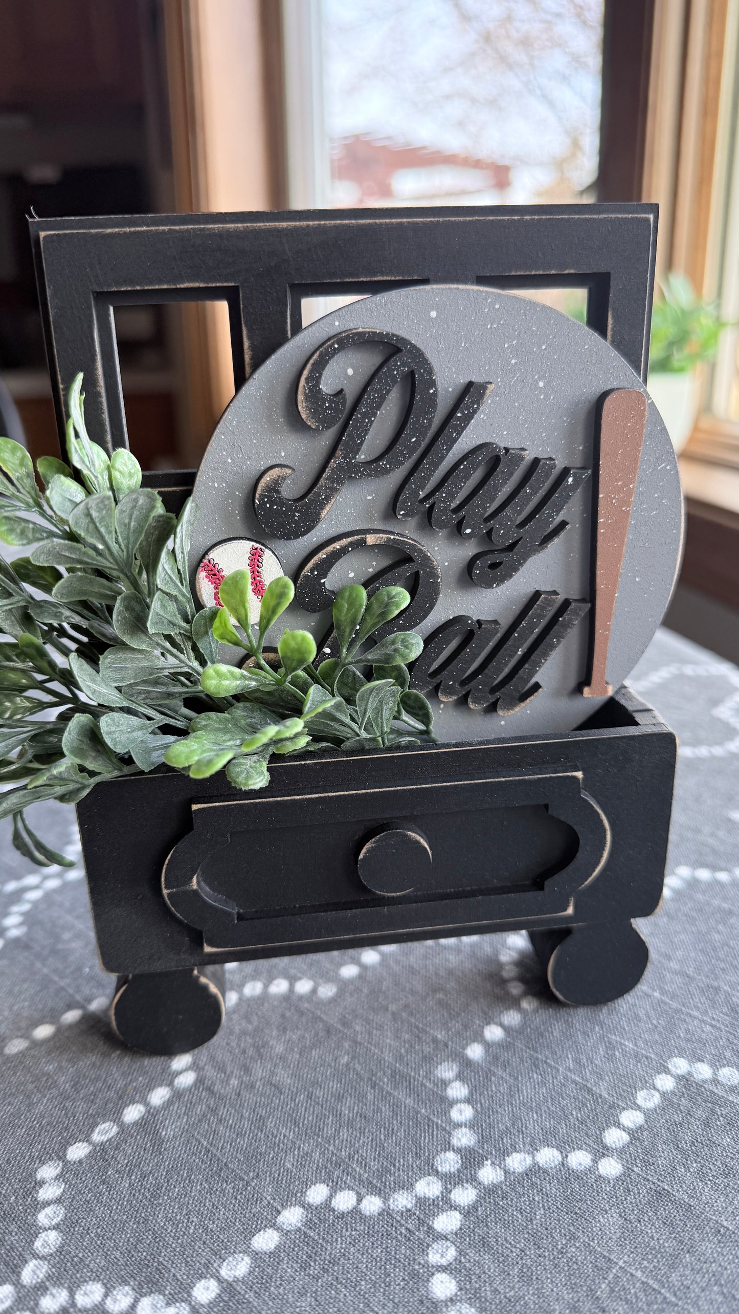 Decorative sign with 'Play Ball' text and greenery on a stand.