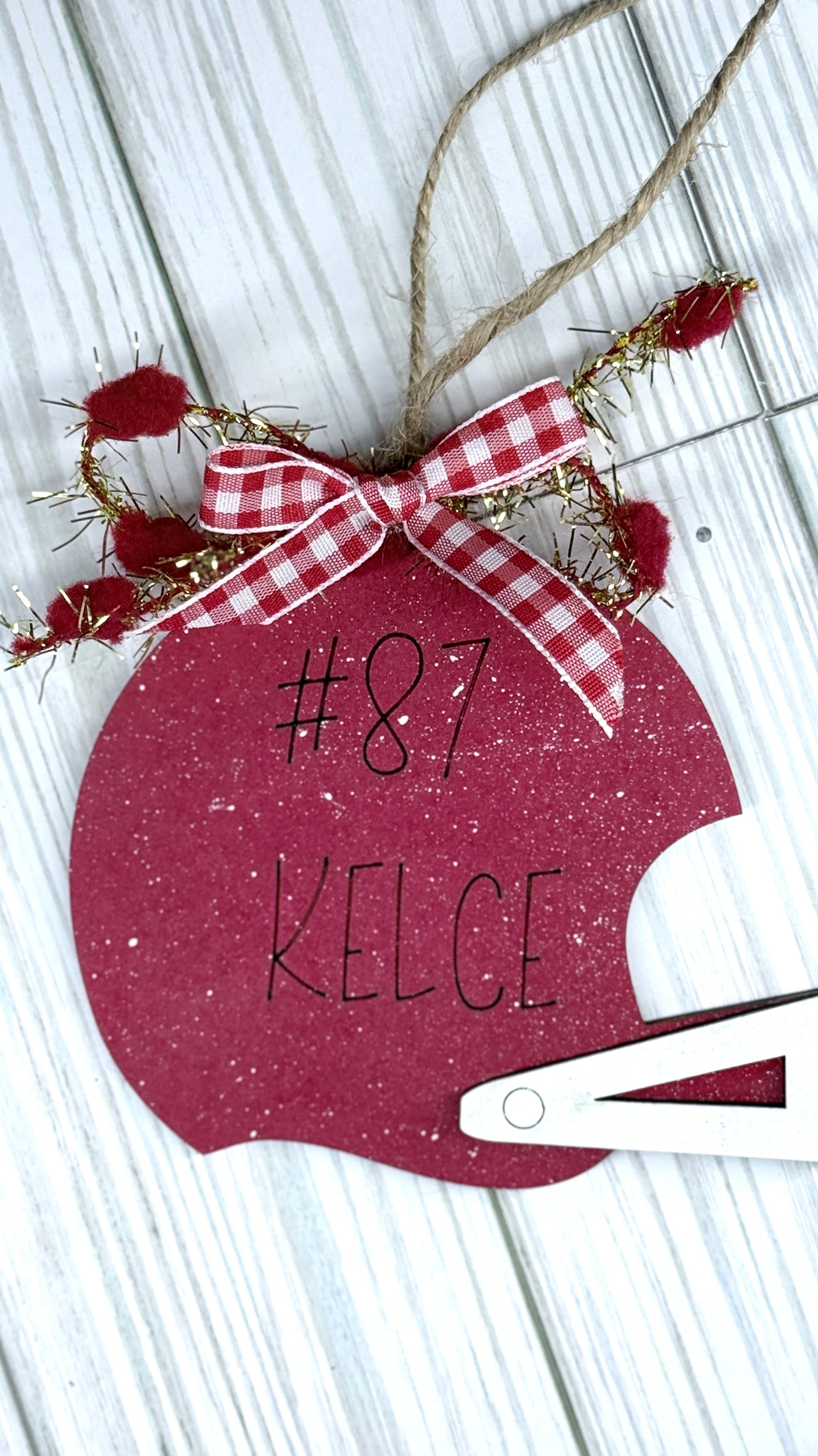 Red ornament with '#87 KELCE' text and a bow on a wooden surface