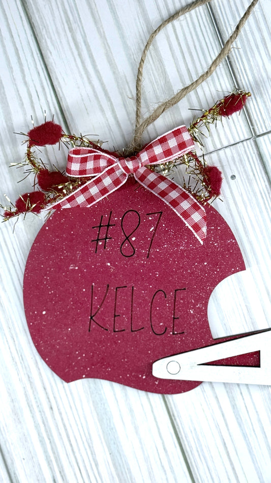 Red ornament with '#87 KELCE' text and a bow on a wooden surface