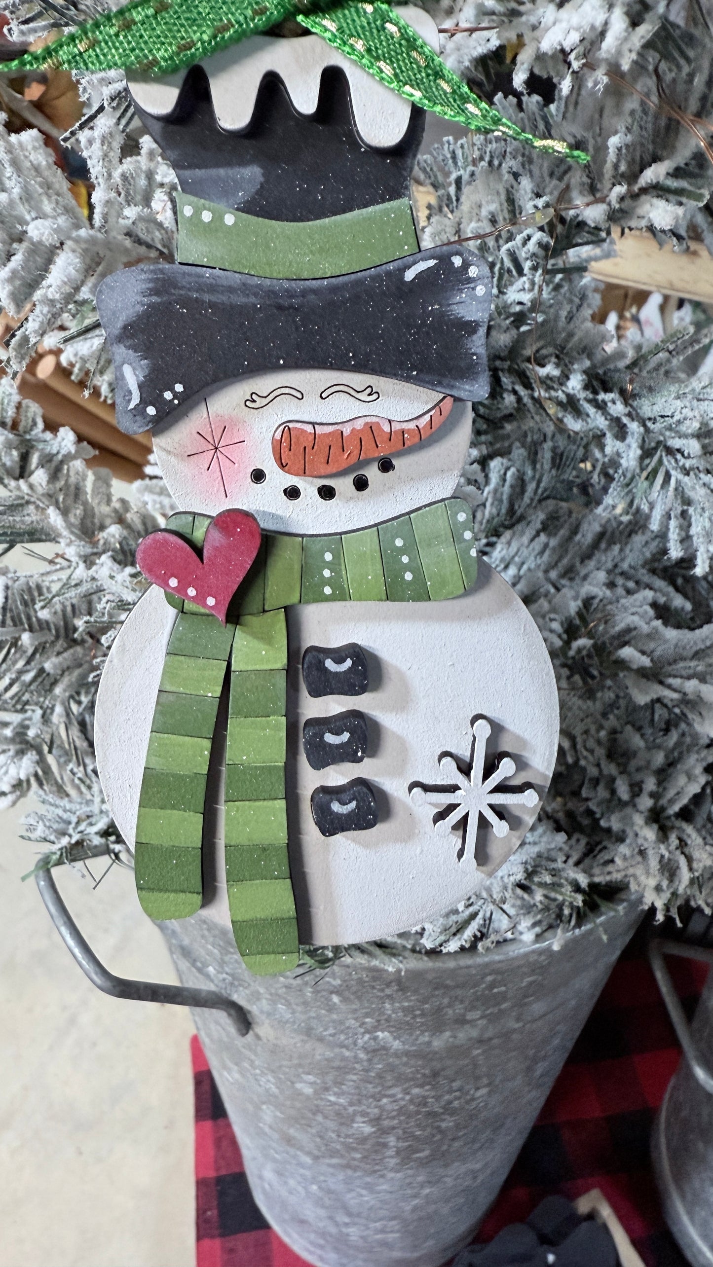 Decorative snowman ornament with a green hat band and scarf, hanging on  a tree