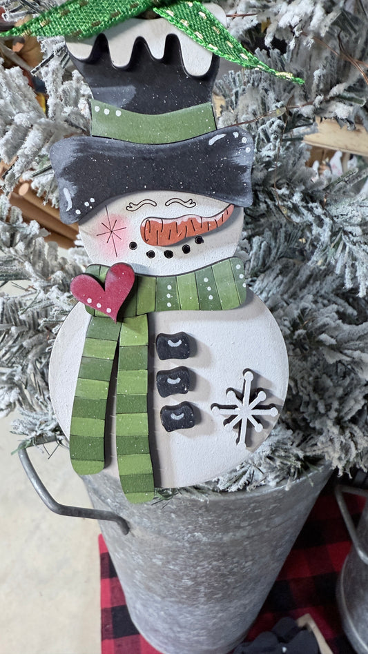 Decorative snowman ornament with a green hat band and scarf, hanging on  a tree
